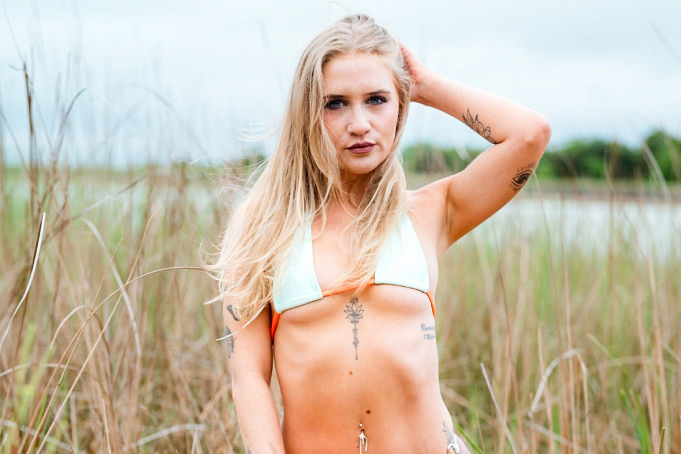 A woman kneeling in a grassy outdoor field wearing a two-piece bikini with a pale mint top.